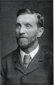 William Doleman - Black and White photograph of a bearded man, from the chest upwards, wearing a dress jacket, white shirt and tie.